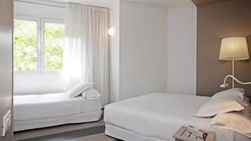 Habitación de hotel con dos camas individuales, una ventana con cortinas, una mesita de noche con lámpara y vistas a zonas verdes.