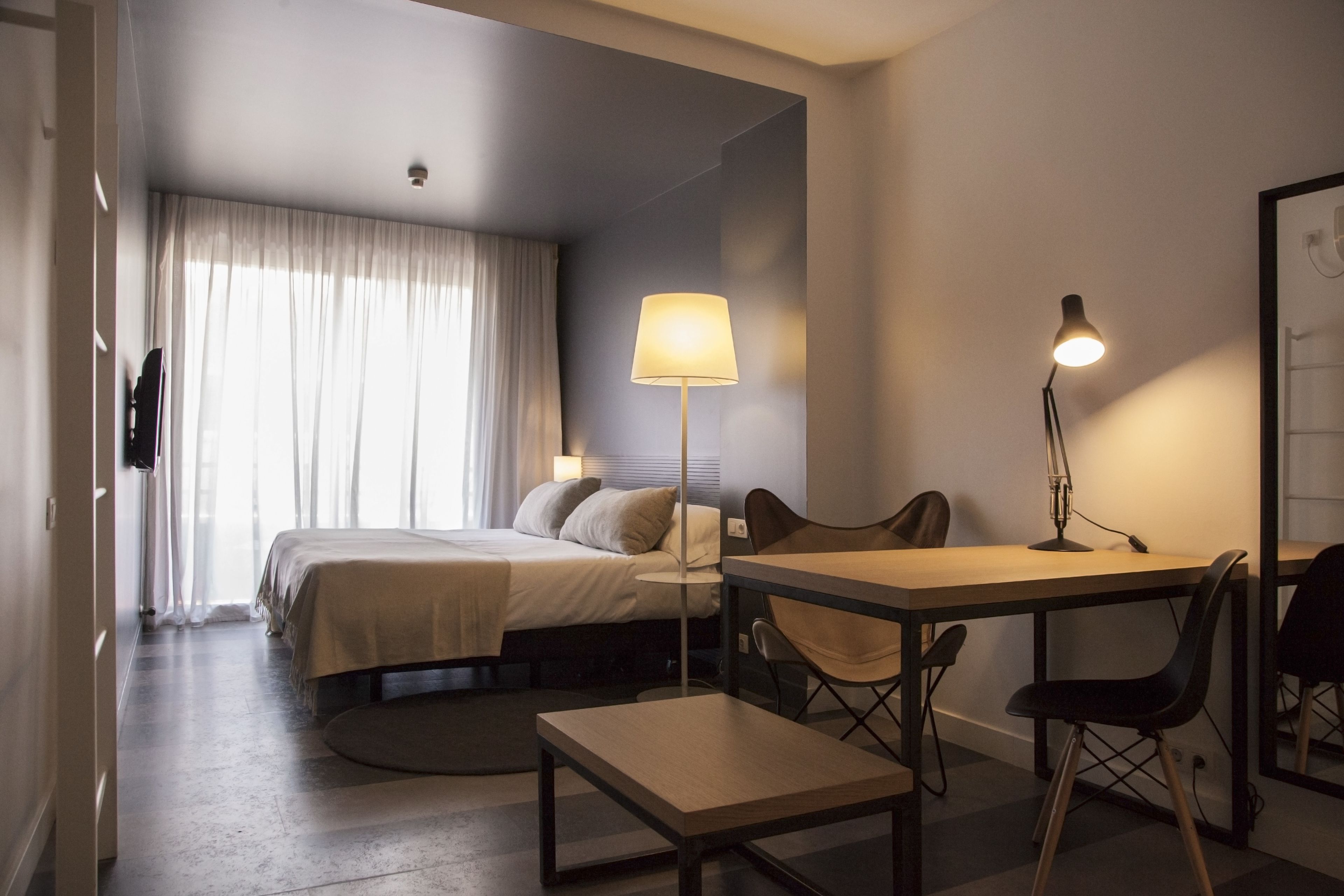 Et moderne hotelværelse med seng, skrivebord, stole og lampe.