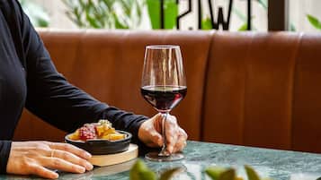 Una persona sentada a una mesa con una copa de vino tinto y un plato de comida.