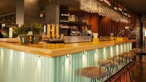 A bar area with a wooden counter, bar stools, and a bartender. - Sixties Ramblas (Barcelona)