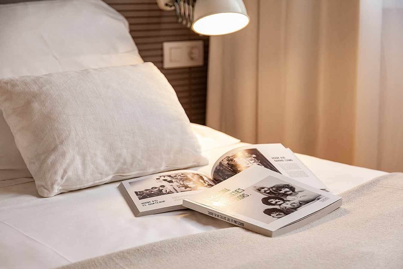 Una cama bien hecha con sábanas blancas, una almohada y un libro encima.