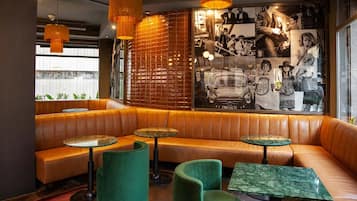 Un salón moderno con asientos de cuero, sillas verdes y mesas redondas.