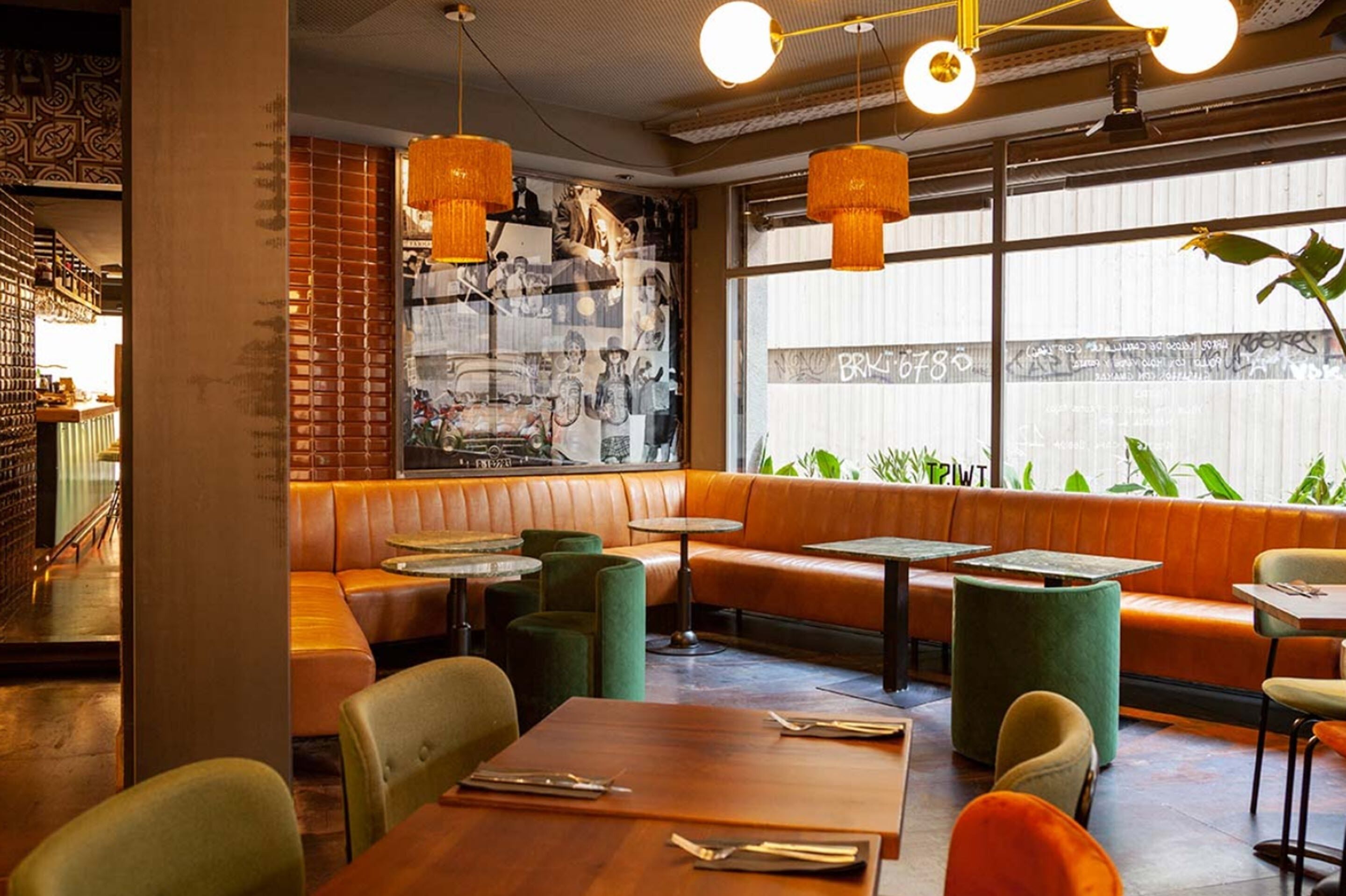 A restaurant interior with a brick wall, green cushioned seating, and pendant lighting.