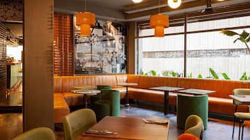 A restaurant interior with a brick wall, green cushioned seating, and pendant lighting.
