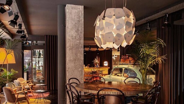 A modern dining area with a round wooden table, dark chairs, and a unique geometric pendant light. - Sixties Ramblas (Barcelona)