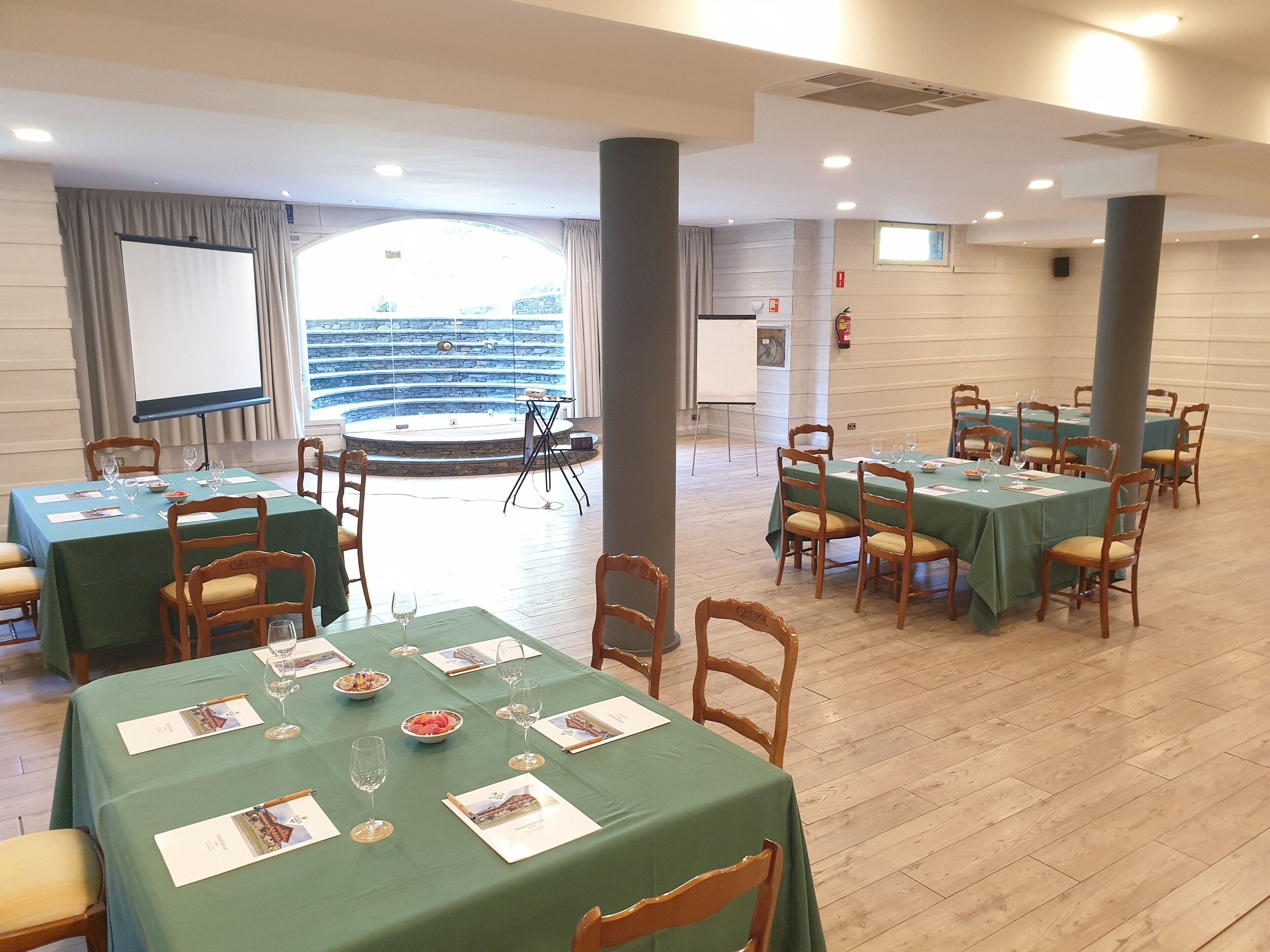 A conference room with multiple tables, chairs, and a large screen.
