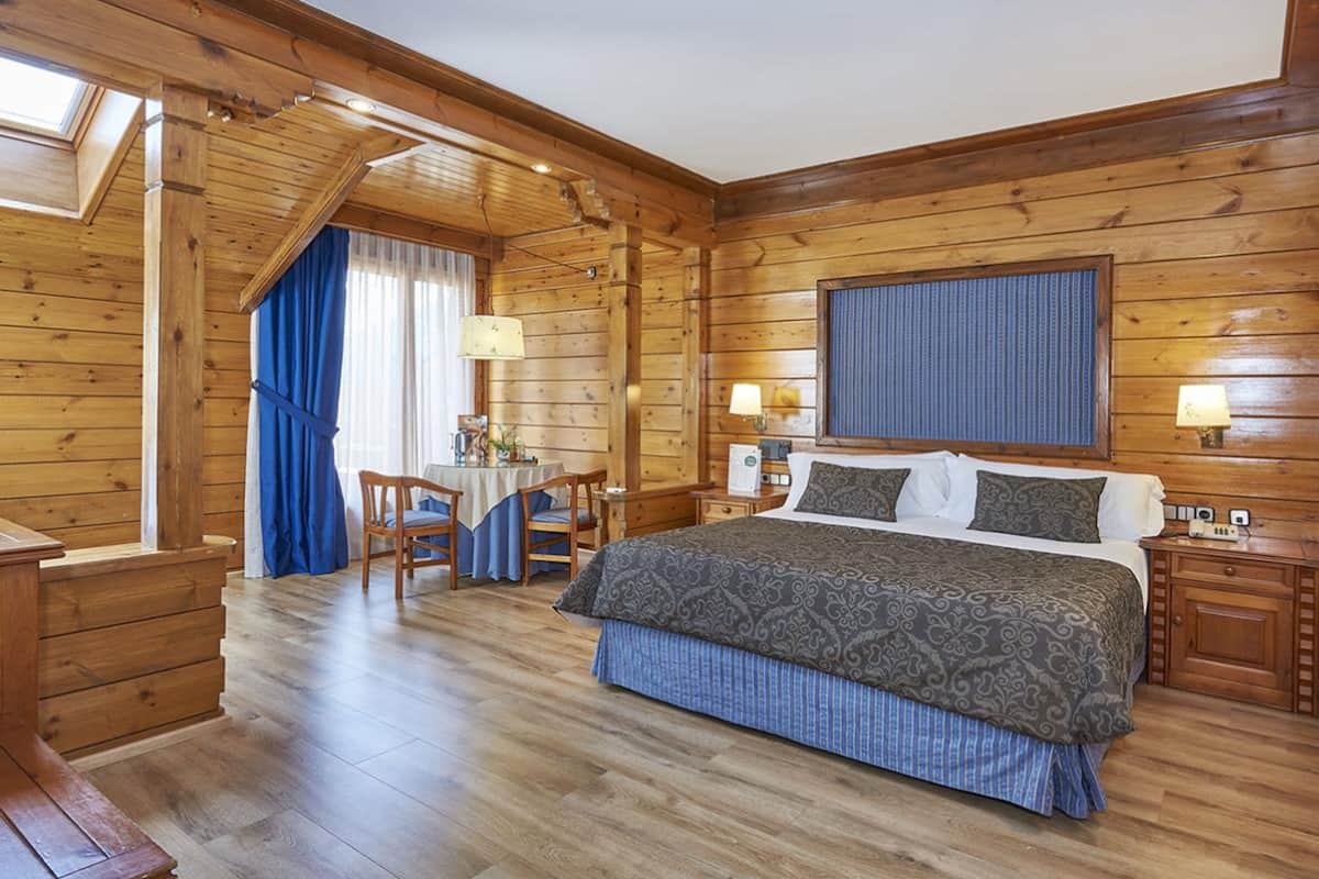Ein schlicht eingerichtetes Schlafzimmer im Chalet-Stil mit einem großen Bett, zwei Nachttischen, einem Schreibtisch mit Stühlen und einem Fenster mit Vorhängen.