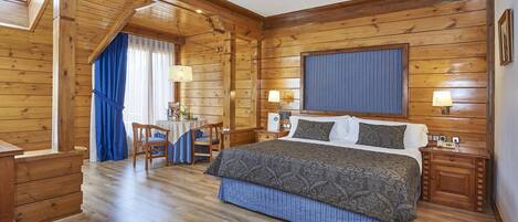 Un dormitorio de estilo cabaña de madera con una cama grande, dos mesitas de noche, un escritorio con sillas y una ventana con cortinas.
