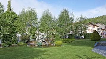 A well-maintained garden with a small pond, neatly trimmed grass, and a variety of trees.