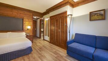 A hotel room with a bed, a blue sofa, wooden paneling, a wardrobe, and a framed picture on the wall.