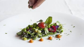 A white plate with a colorful salad and a hand sprinkling herbs.