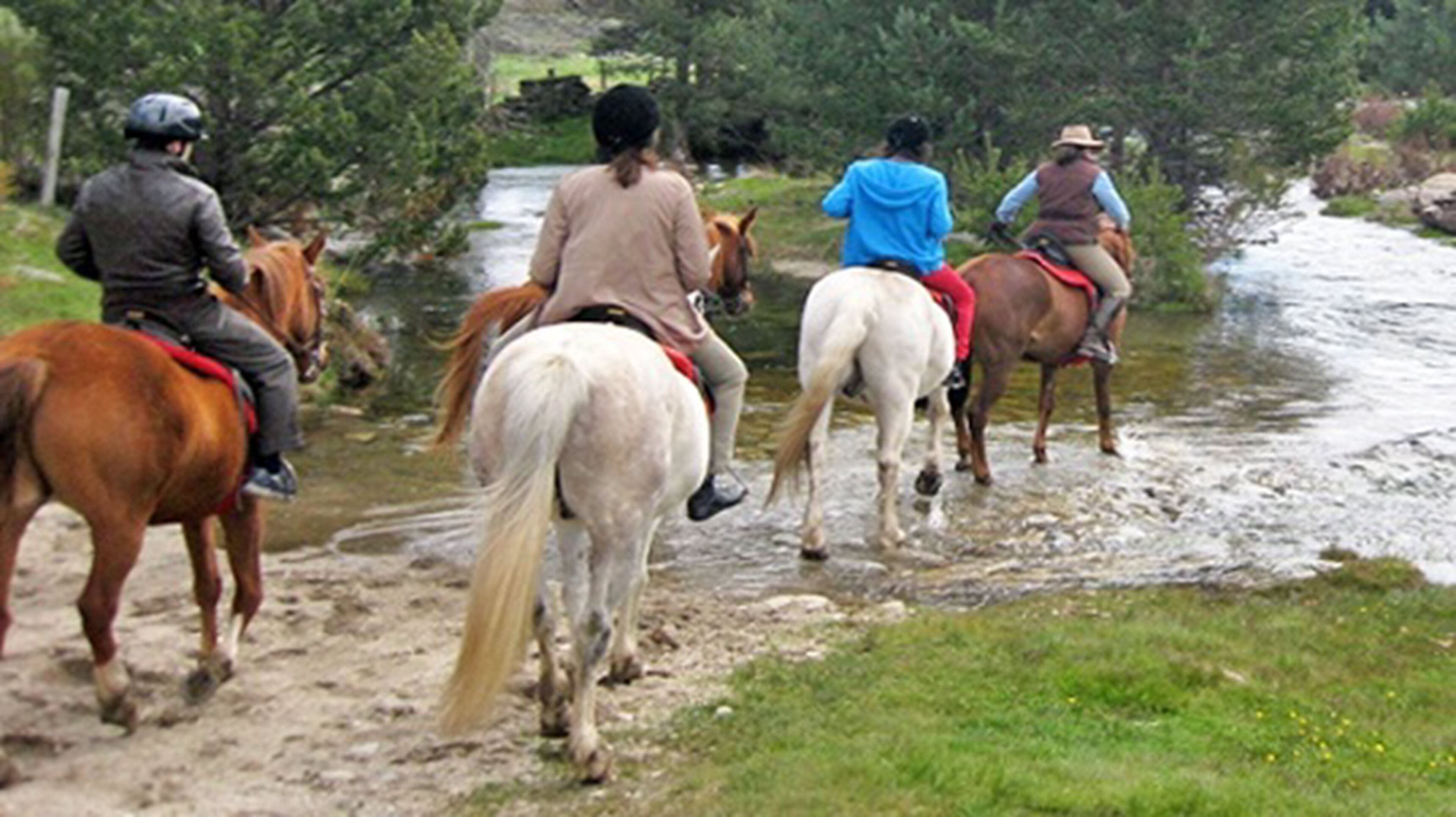 A group of people riding horses along a river path.