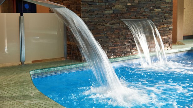 A pool with two water features, a stone wall, and a tiled floor.