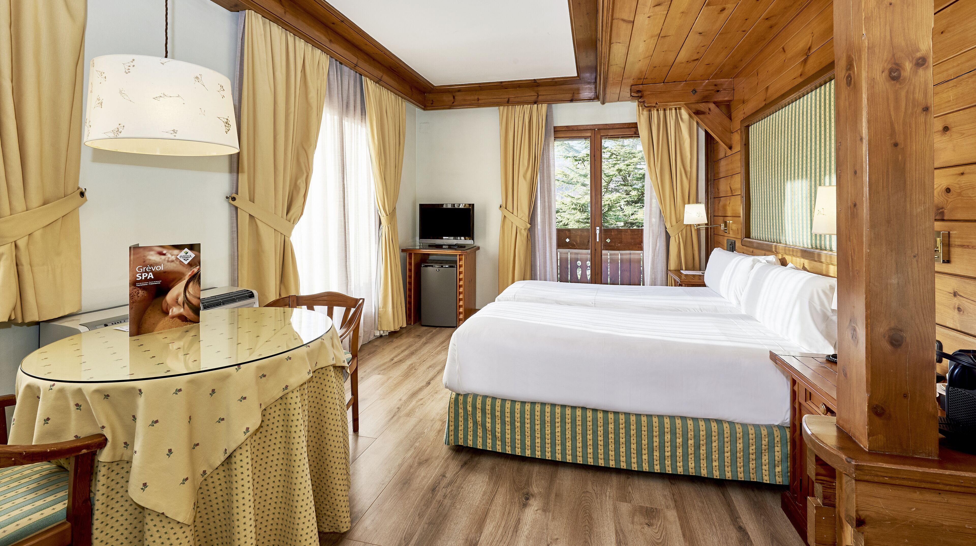 A hotel room with a large bed, a small desk with a television, a dining table, and curtains.