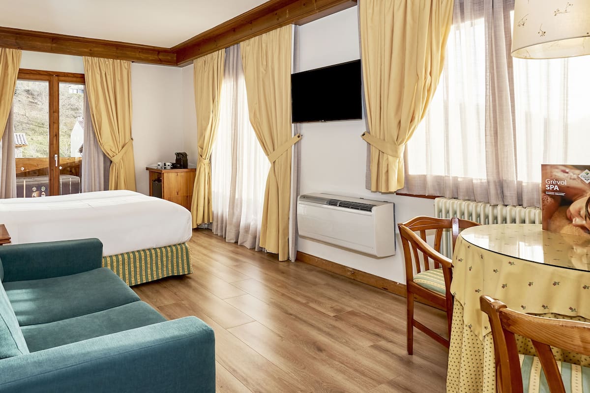 Ein Hotelzimmer mit Bett, Sofa, Tisch, Stuhl, Klimaanlage und Vorhängen.