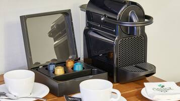 A coffee maker with a cup and saucer, a spoon, and a napkin on a table.
