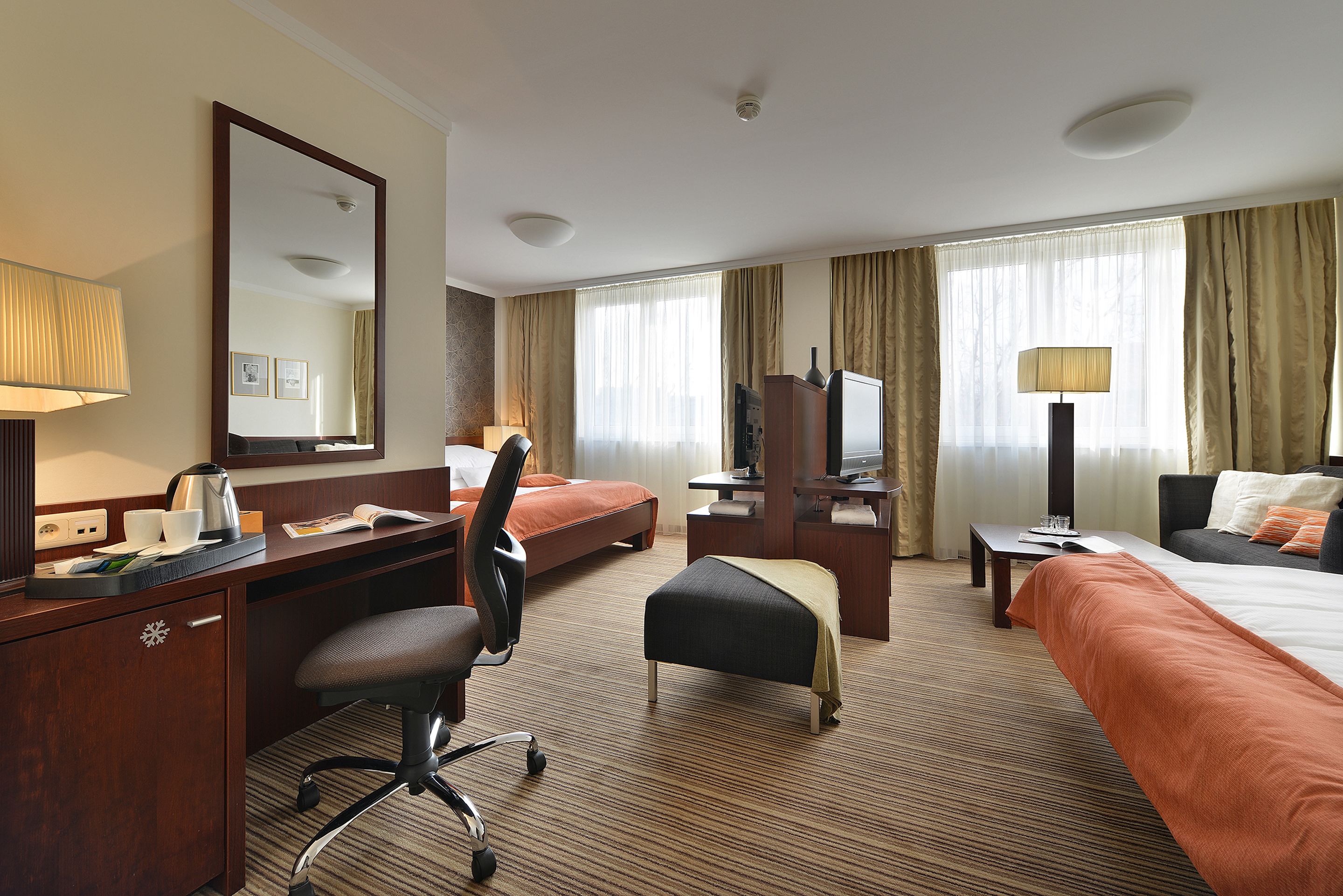 A hotel room with a desk, two beds, a chair, a TV, and a mirror.