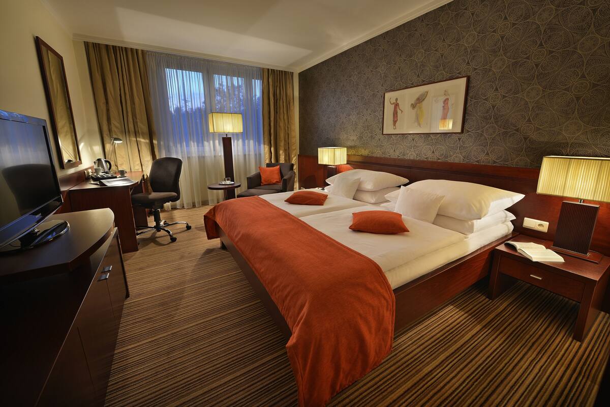 A hotel room with a large bed, two bedside tables, a desk with a computer, a chair, and a television.