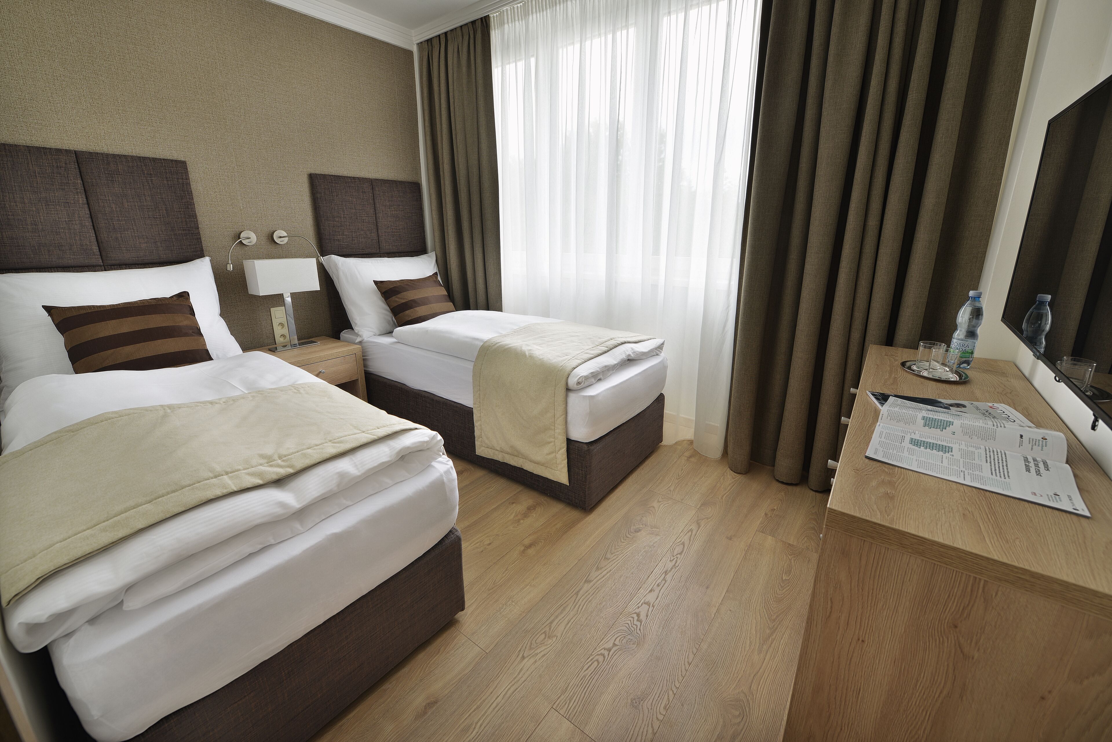 Una habitación de hotel con dos camas, un escritorio de madera, una lámpara y una ventana con cortinas.