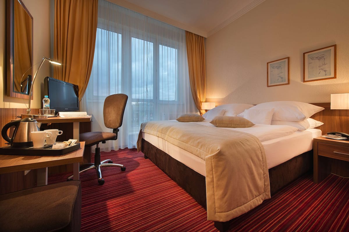 A hotel room with a bed, desk, chair, and a large window with curtains.