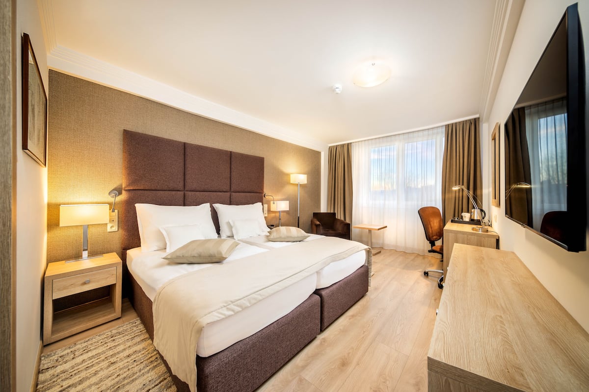 A hotel room with a large bed, bedside tables, a desk, and a TV.