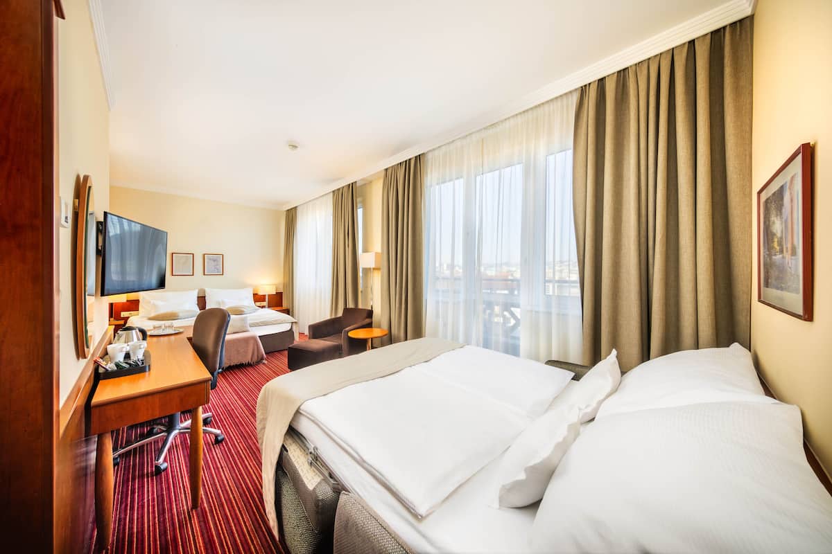 A hotel room with a large bed, a desk with a chair, a television, and a window with curtains.