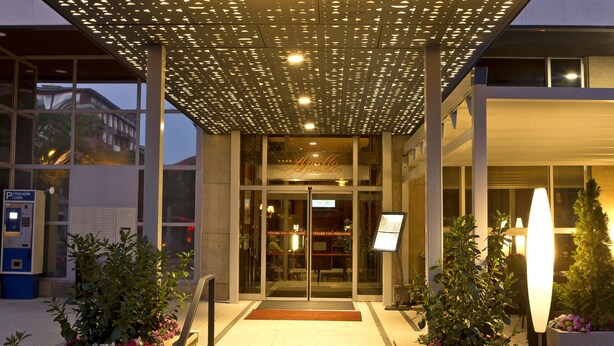 Entrada del Hotel Apollo con un paseo techado, escalones que conducen a la puerta y macetas con plantas a ambos lados.