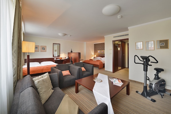A hotel room with a bed, two sofas, a coffee table, a desk, a lamp, and an exercise bike. - Apollo Hotel Bratislava (Bratislava)