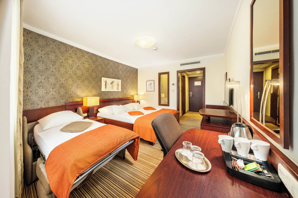 A hotel room with two beds, a dining table with a tray of cups and a kettle, and a mirror reflecting the room.