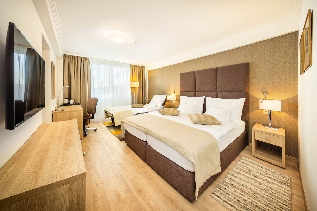 A hotel room with a large bed, a desk, a chair, a TV, and a window with curtains.