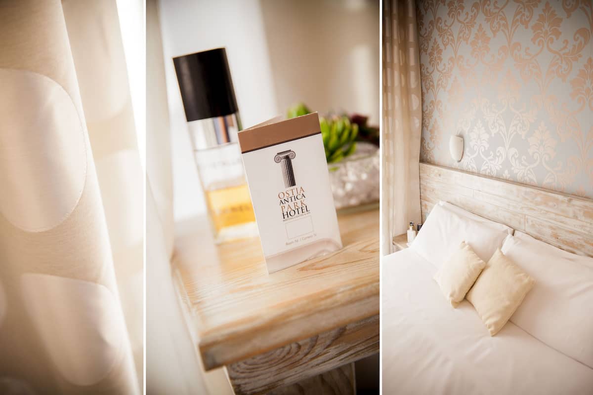 A hotel room with a wooden headboard, a bed with white linens, and a nightstand with a book titled "OSTIA ANTICA PARK HOTEL."