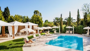 Un espace piscine agrémenté de chaises longues et de parasols, entouré de verdure et d’arbres.