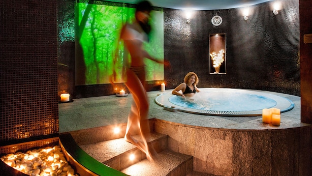 Un espace détente avec un jacuzzi, des bougies et une projection d’un paysage forestier sur le mur.