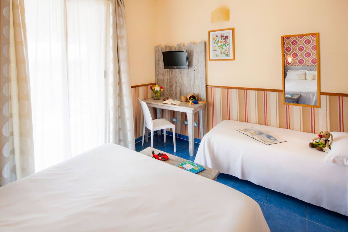 A hotel room with two beds, a desk with a chair, a television, and a mirror.