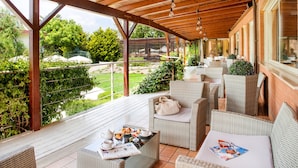 Un espace extérieur aménagé, abrité et doté de mobilier en osier, d’une table avec un journal et d’une vue sur le jardin.
