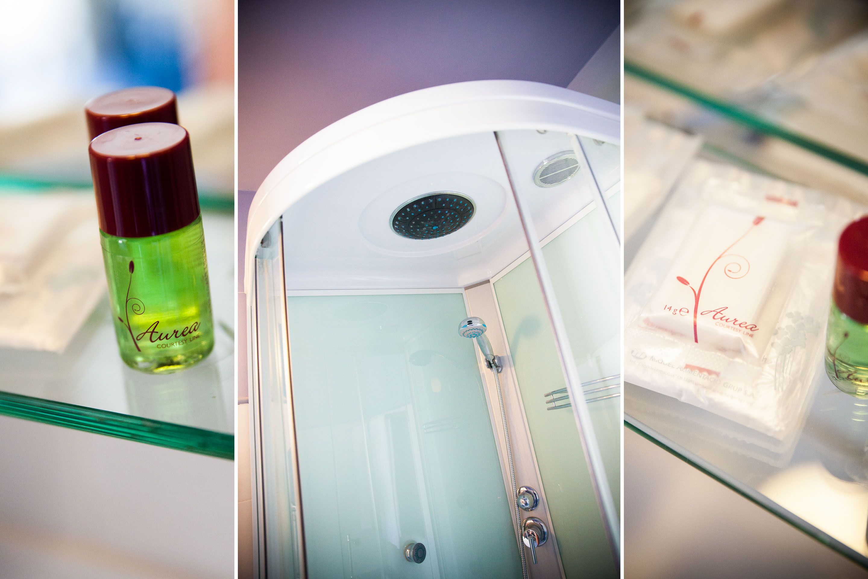 Ducha con cerramiento de vidrio, con panel de control, una botella y un paquete de gel de baño Aurea sobre un estante de vidrio.