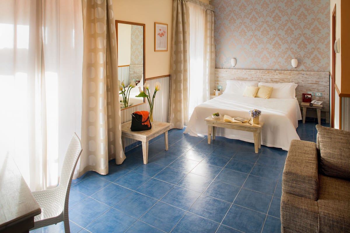 A hotel room with a bed, a small table, a chair, and a sofa.
