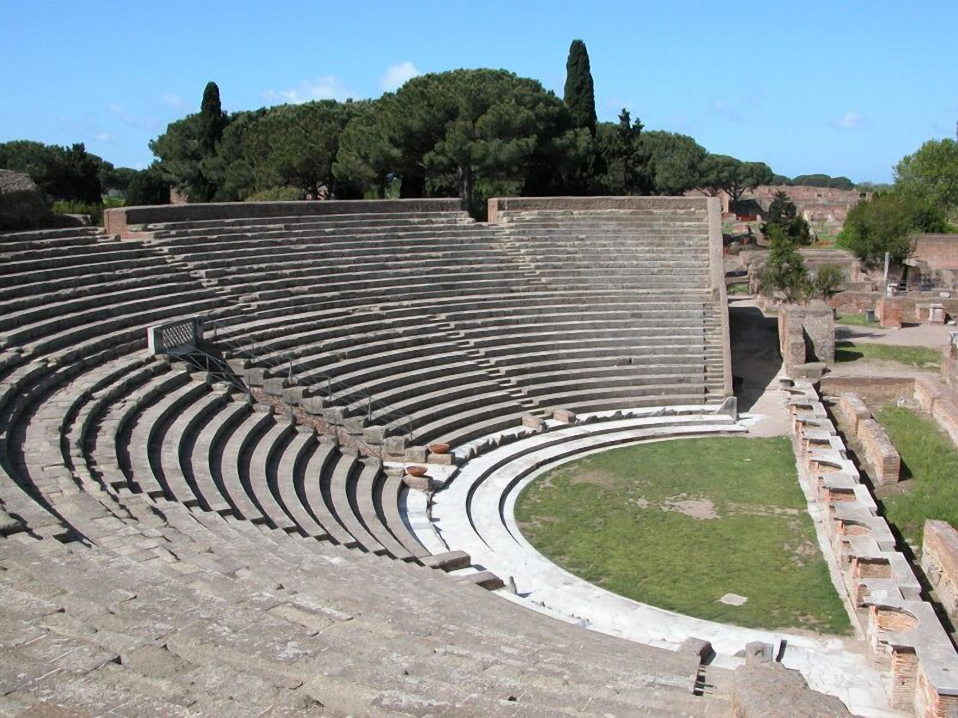 An ancient amphitheater with tiered seating and a central stage area.