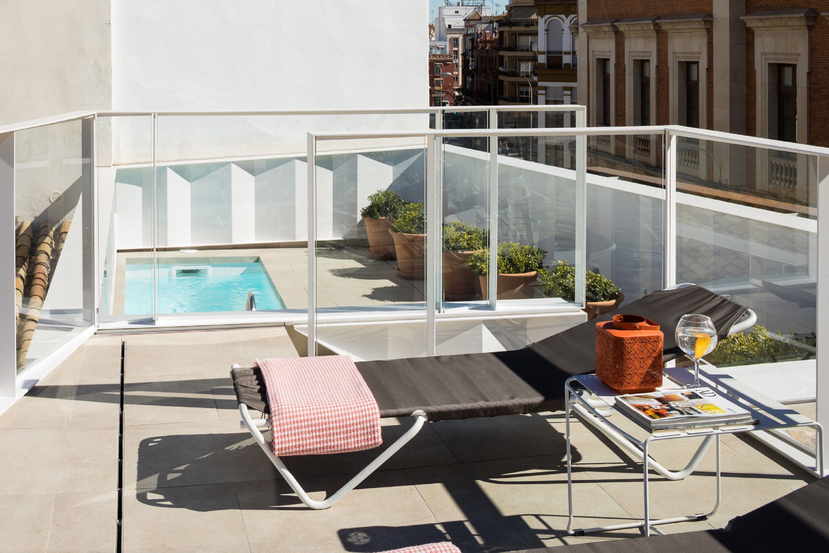 A balcony with a pool, lounge chairs, and potted plants.