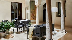 A spacious indoor area with a modern seating arrangement, including sofas and chairs, under a series of arches. There are potted plants and a large painting on the wall. - Hotel Posada del Lucero (Seville)