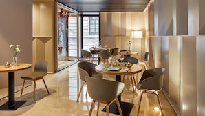 A modern dining area with round tables, chairs, and a view of the street outside. - Hotel Posada del Lucero (Seville)