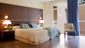 A modern hotel room with a large bed, two bedside lamps, a chair, and a view of the city through a window. - Hotel Rice Palacio de los Blasones (Burgos)