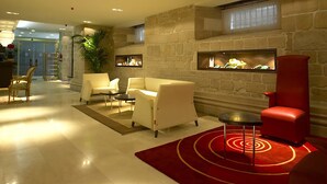 A modern lobby with a stone wall, a red armchair, a white sofa, and a small table. - Hotel Rice Palacio de los Blasones (Burgos)