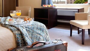 A hotel room with a bed, a desk with a computer, a chair, a view of a cathedral, and breakfast items on the bed. - Hotel Rice Palacio de los Blasones (Burgos)