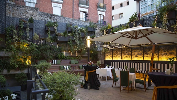 An outdoor patio area with tables and chairs, surrounded by greenery and a stone wall. - Hotel Rice Palacio de los Blasones (Burgos)