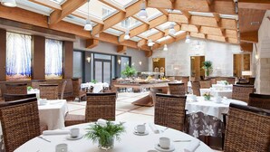 A spacious dining area with high wooden beams and skylights, wicker chairs, and tables set for dining. - Hotel Rice Palacio de los Blasones (Burgos)