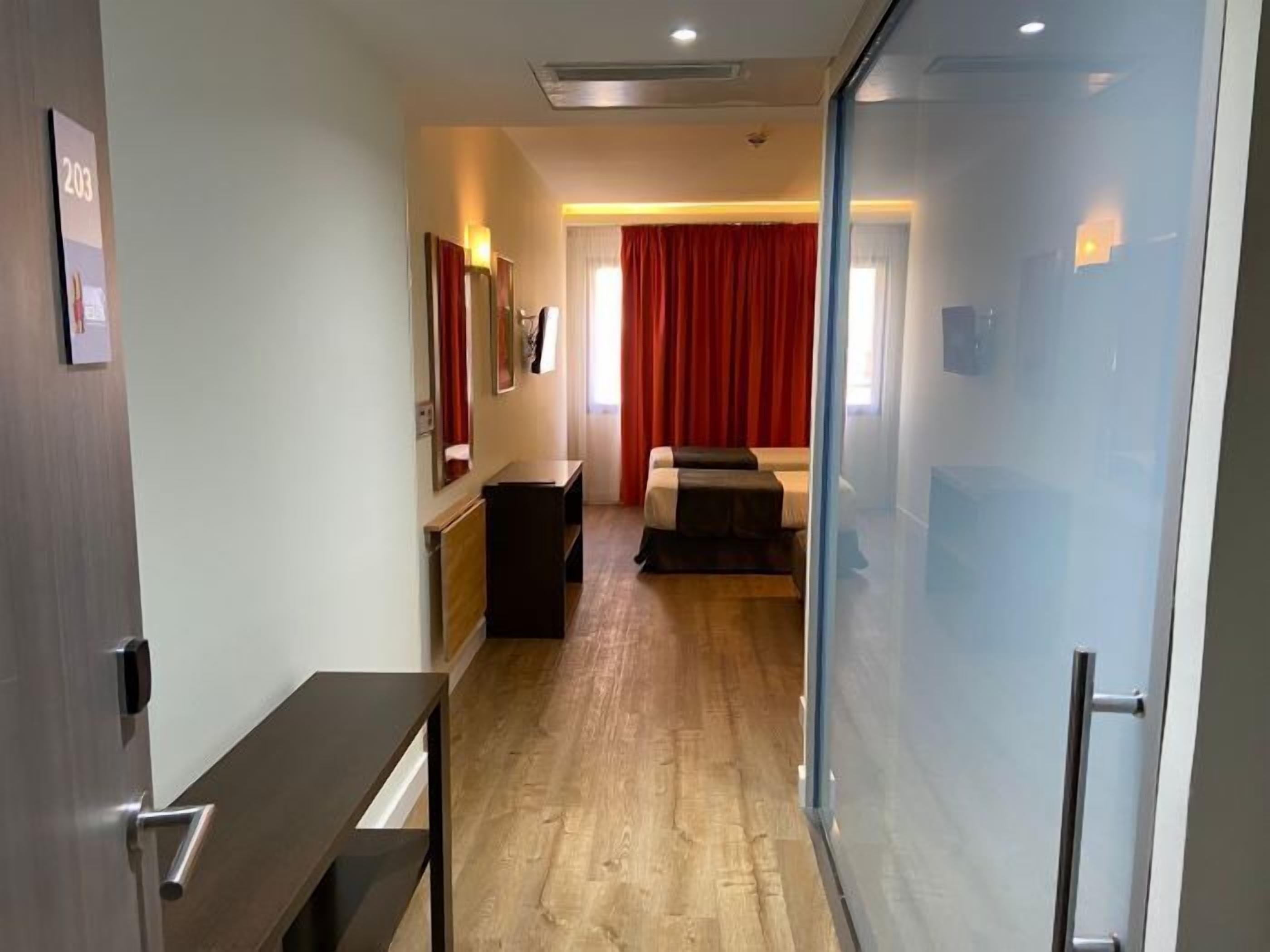 Una habitación de hotel con piso de madera, una cama, un escritorio y un separador de vidrio.