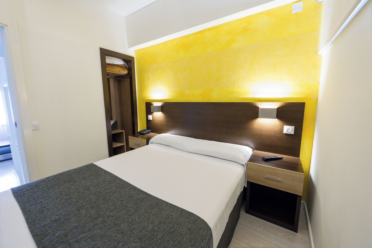 A hotel room with a bed, bedside tables, a nightstand, a lamp, and a wardrobe.