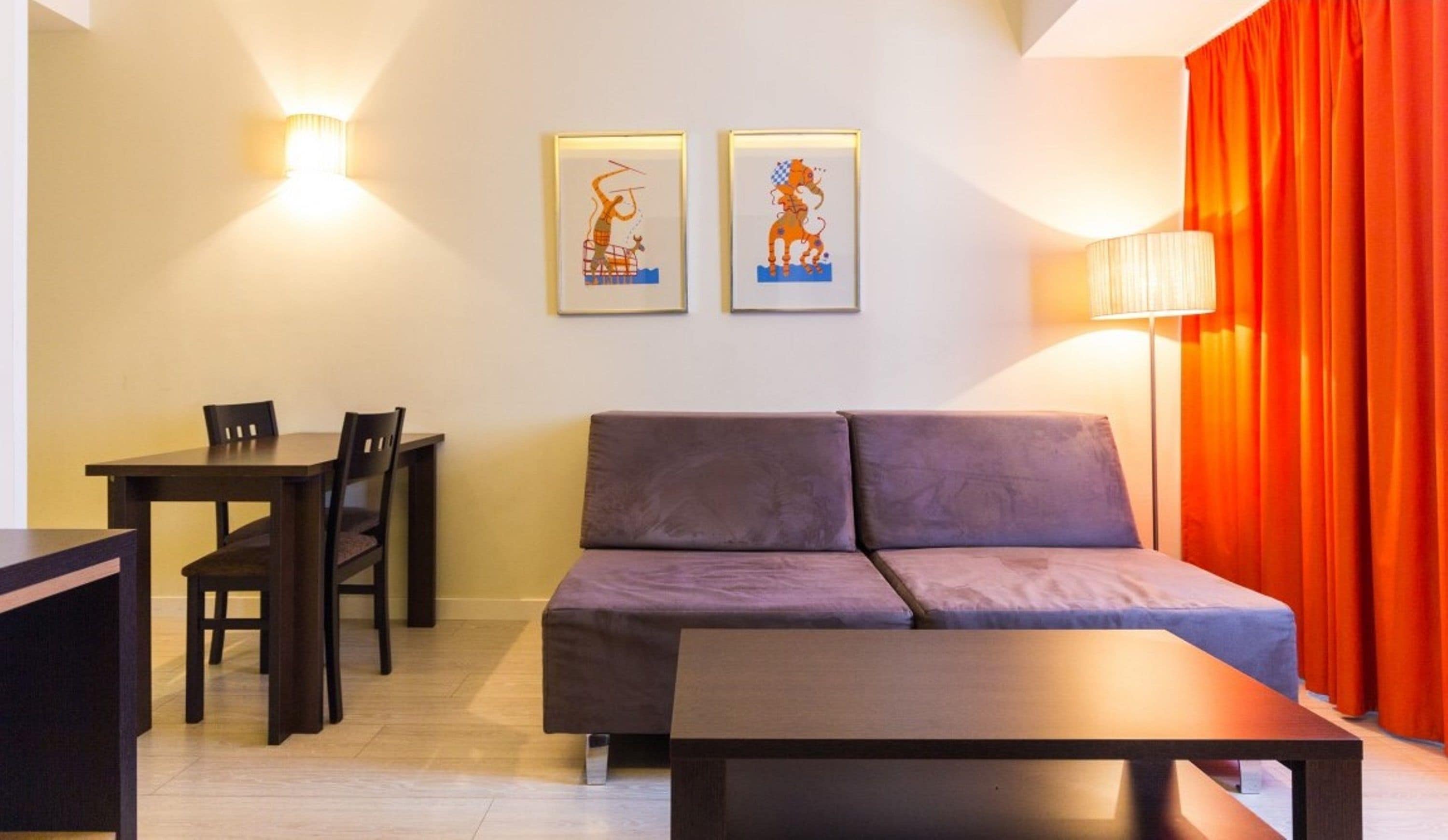 A modern living room with a sofa, a dining table with chairs, and two framed artworks on the wall.