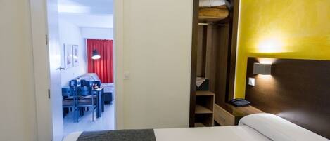 Ein Hotelzimmer mit Bett, Schreibtisch, Stuhl, Kleiderschrank und einer kleinen Schreibtischlampe.